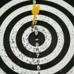 Close-up of a dart hitting the bullseye on a black and white target board symbolizing success.